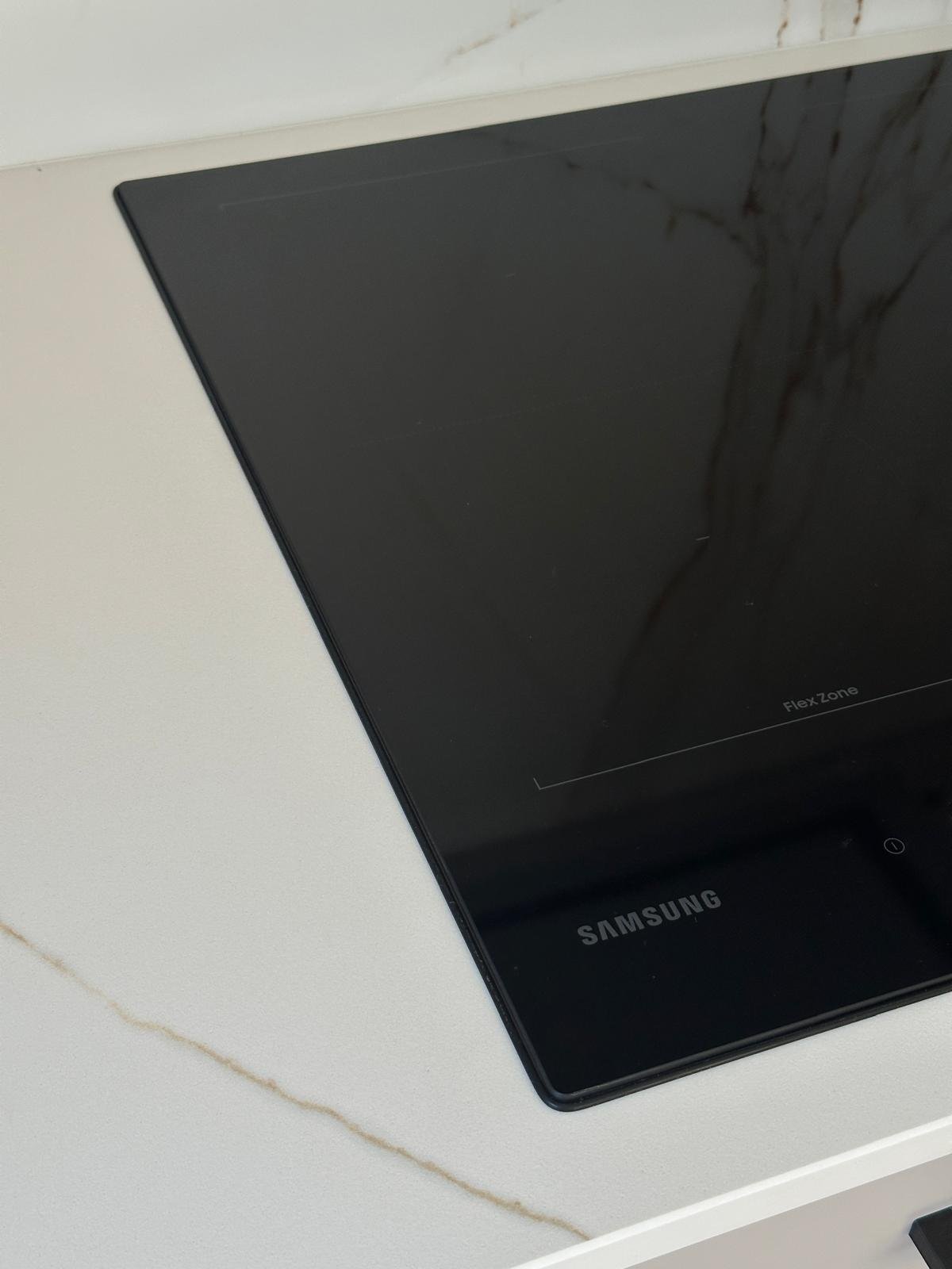Płyta indukcyjna Samsung z Flex Zone na marmurowym blacie, z czarną uszczelką CleanCook wzdłuż krawędzi szkła
